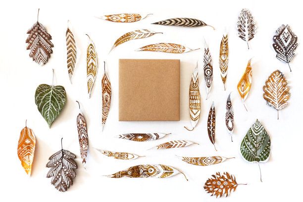 干枯的涂过漆的树叶中间放着一个方形的牛皮纸盒子。图片下载