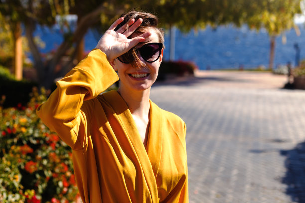 穿着裙子的女孩微笑着沿着海边散步。这张照片是在一个阳光明媚的日子里在海边拍的。照片上的女孩穿着黄色连衣裙，戴着大大的黑色太阳镜。图片下载