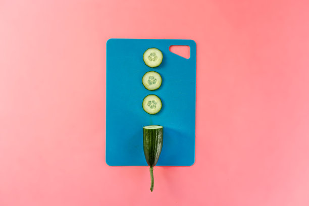 新鲜的黄瓜切片放在蓝色的砧板上，粉红色的背景图片下载