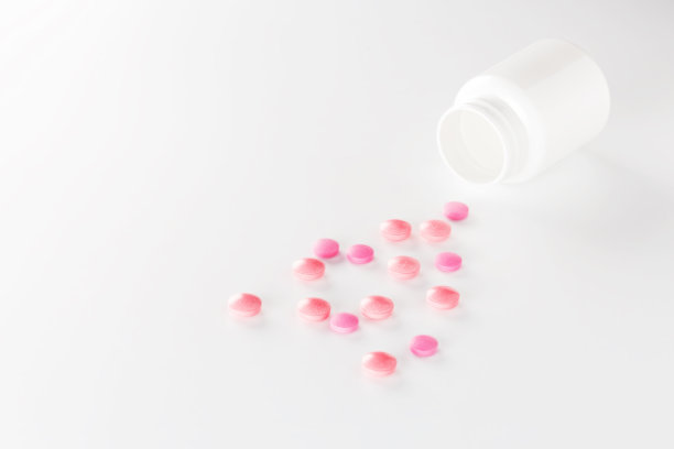 一堆红色的药丸和塑料白色的瓶子。药丸在白色的背景。保健和医学的概念。图片下载