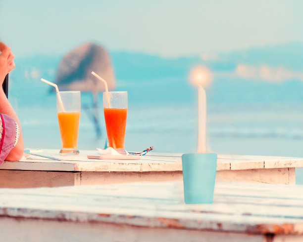 女人的手，两杯新鲜的果汁，燃烧的蜡烛在木桌上的咖啡馆在海滩上。图片下载