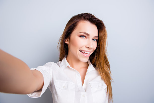 有问题的狂热!好性感，好漂亮!有魅力的年轻女子正在相机上自拍，轻浮而好玩。在休闲装上，以纯光为背景图片下载