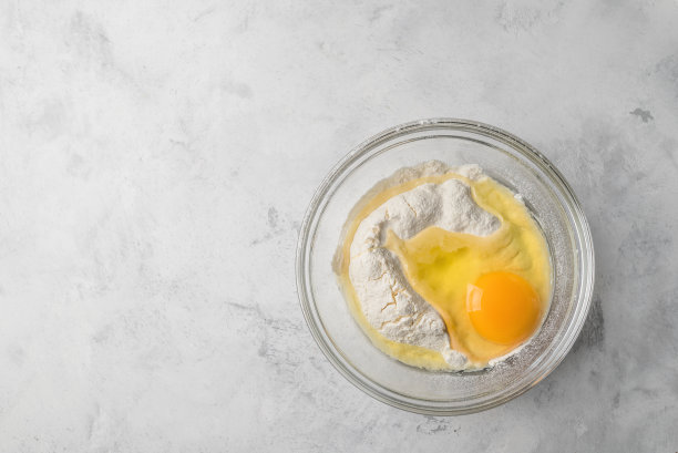 俯视图照片，一个碎鸡蛋在面粉在玻璃盘子。图片下载