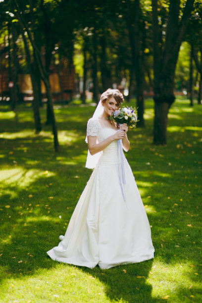 美丽的婚礼photosession。优雅的年轻新娘穿着白色的裙子和面纱，美丽的发型和花束和丝带在婚礼散步在大的绿色公园在阳光明媚的一天图片下载