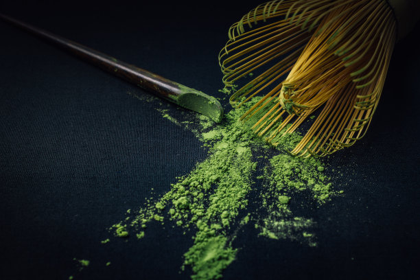 把竹打蛋器和抹茶绿茶粉放在黑色的背景上。图片下载