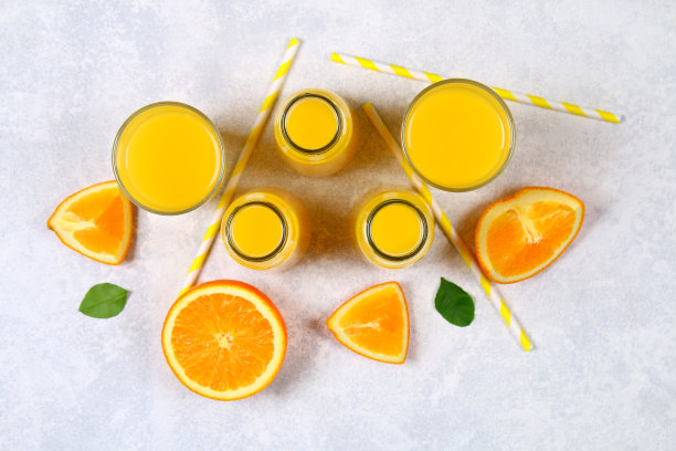 浅灰色的桌子上放着玻璃瓶、玻璃杯和一罐新鲜的橙汁，橙汁和黄色的管子被切成薄片。前视图。平的。图片下载