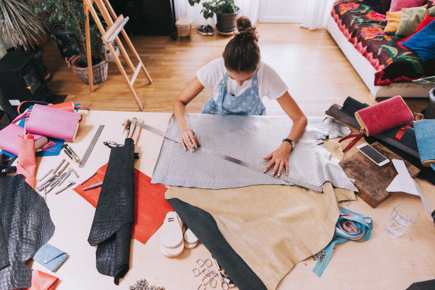年轻女性钱包制造者在她的车间与皮革纺织工作。图片下载