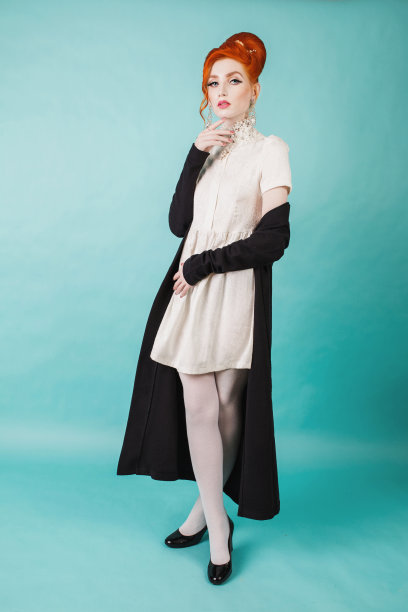 美丽的红发女人与复古发型和化妆在一个黑色的卡片外套在一个蓝色的背景。红发白裙黑鞋模特图片下载