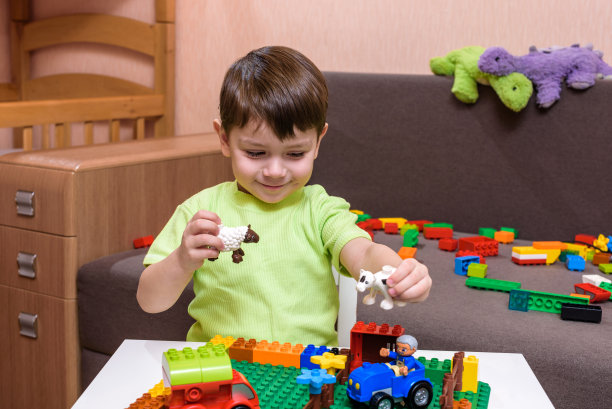 白人小孩在室内玩五颜六色的塑料积木。穿着衬衫的小男孩，玩着建筑创造图片下载