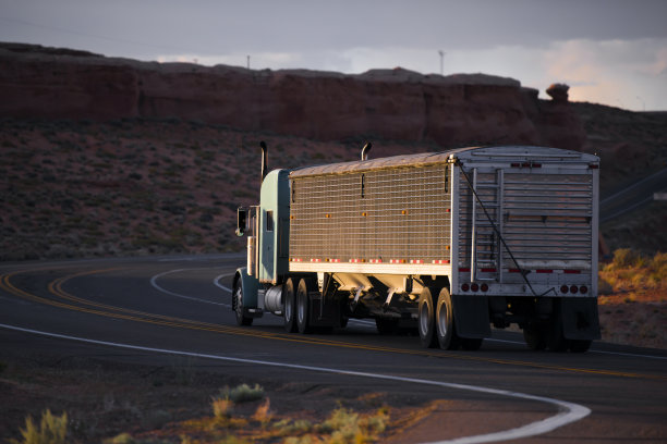 大卡车半挂车与散装覆盖半挂车走在蜿蜒的道路与红色岩石亚利桑那景观在黄昏图片下载