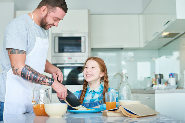 快乐的父亲把煎蛋放在女儿的盘子里图片下载