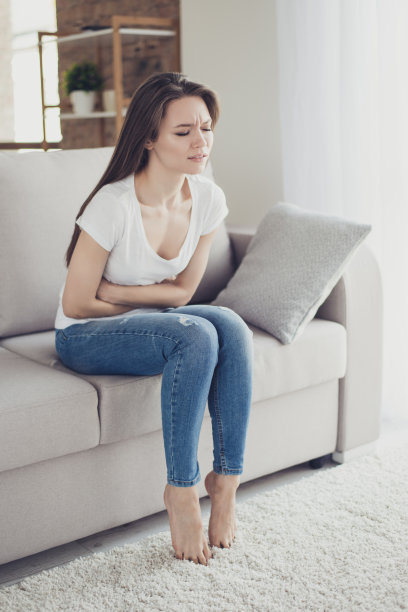心烦意乱的漂亮女人坐在沙发上，感觉痉挛和经前综合症的症状图片下载