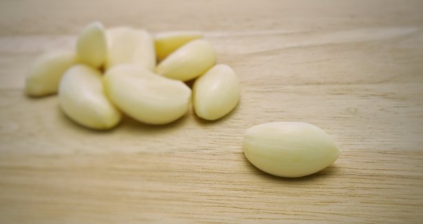 一张剥皮的蒜瓣放在木桌上，背景是一堆模糊的大蒜。图片下载