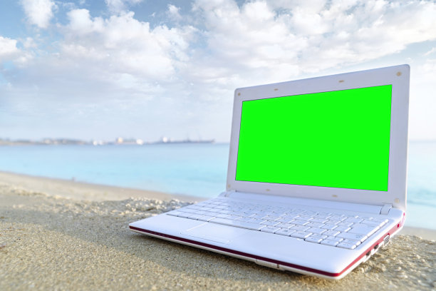 空的绿色屏幕笔记本电脑在沙滩上，以大海为背景。用于图形和产品显示蒙太奇。夏日沙滩概念图片下载
