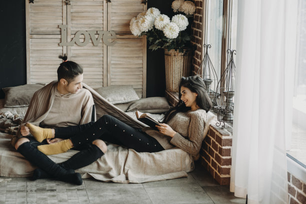 年轻的女孩正在读书，与她的爱人坐在一个温馨的房间里。图片下载