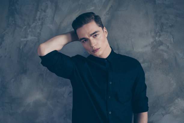 近距离的肖像年轻非常可爱的男人模特在黑色的服装。他严肃的脸，摸着脖子，身后是灰色的背景图片下载