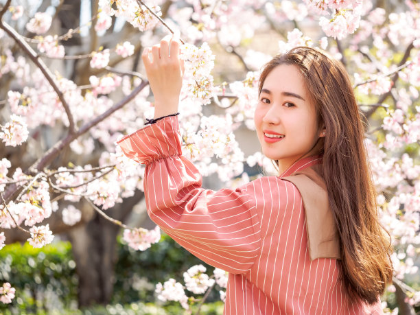 户外肖像美丽的年轻的中国女孩在春天的花园樱花树早午餐微笑，美丽，夏天，情感，表达和人们的概念。素材图片