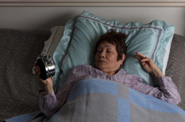 夜间躺在床上看闹钟的不安分的资深女性图片下载