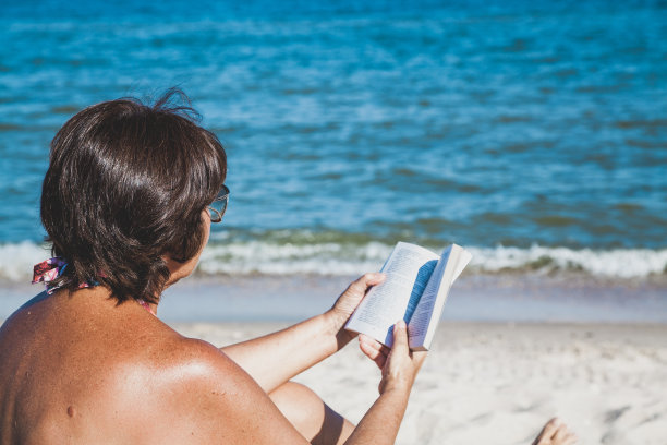一位老妇人在海滩上看书图片下载