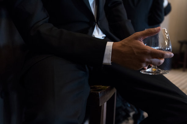 穿着燕尾服的男人抓着一杯威士忌。图片下载
