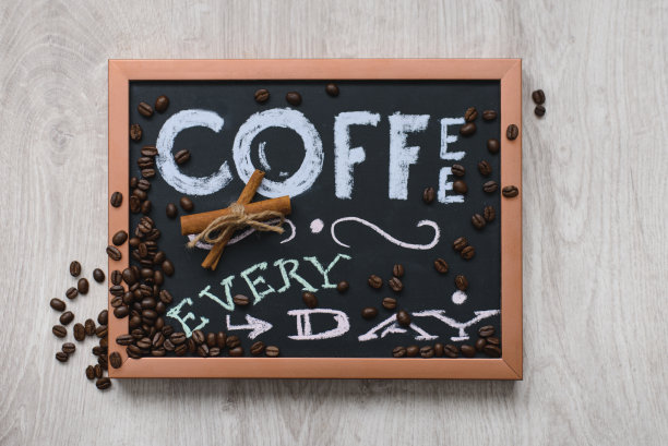 有铜框架的石板，肉桂棒，每天用粉笔写的字和在木制背景上的咖啡豆的静物画图片下载