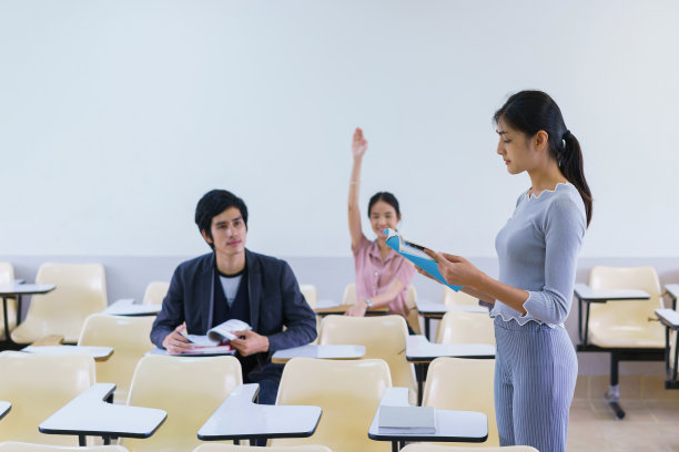 年轻女子站在一个教室里的朋友学生展示准备好的答案。教育的概念。图片下载