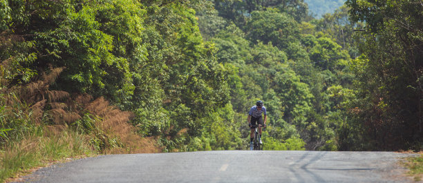 亚洲男人在早上骑公路自行车。他在一条森林道路上。图片下载