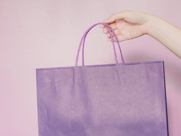 商业，金融和购物的概念，从美丽的女人手握紫色蜡笔纸购物袋的右手与粉色蜡笔孤立的背景图片下载