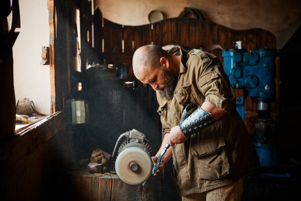 工人用砂轮在磨床上磨制金属零件。旧的磨床是固定在树干上锯断的图片下载