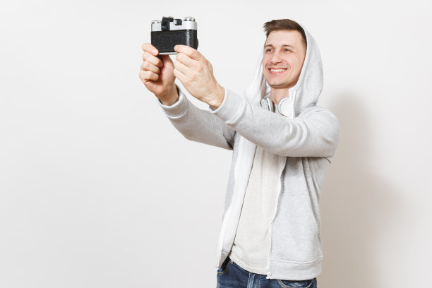 年轻英俊的微笑男学生在t恤和轻运动衫兜帽与耳机照片自己在复古相机孤立的白色背景。摄影概念，爱好图片下载
