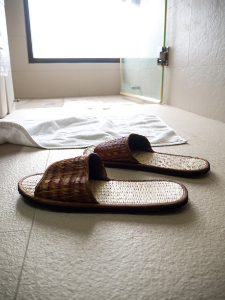 浴室地板上的拖鞋后面是一块白布放在淋浴器前面图片下载