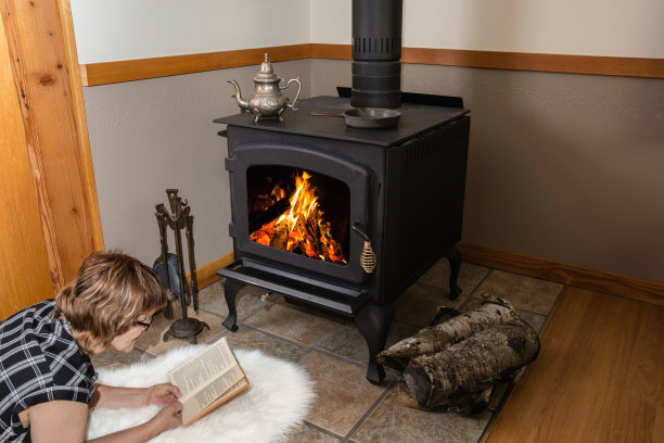 女人躺在地板上，在烧木头的火炉旁看书。图片下载