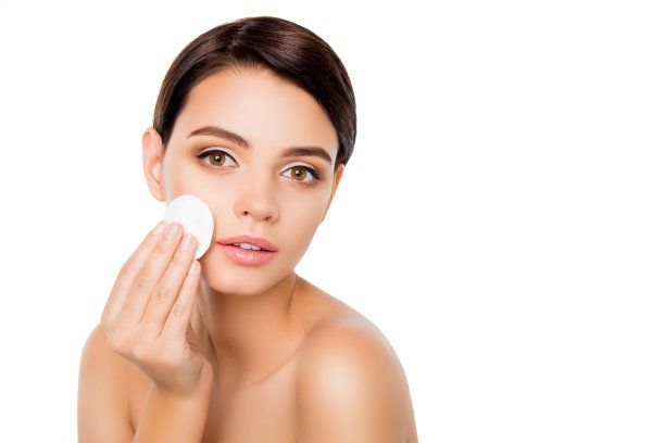 一个年轻美丽的女人在孤立的白色背景使用卸妆棉从她的脸上图片下载
