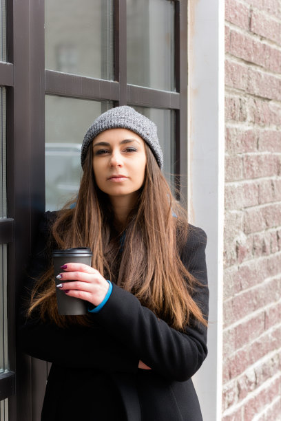 女人灰色的针织帽，黑色的外套，配咖啡去杯图片下载