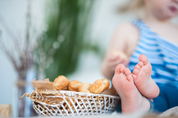 一个穿背心的小女孩穿着背心坐在桌子上。重点关注孩子们的腿和一个盛着牛角面包的篮子图片下载