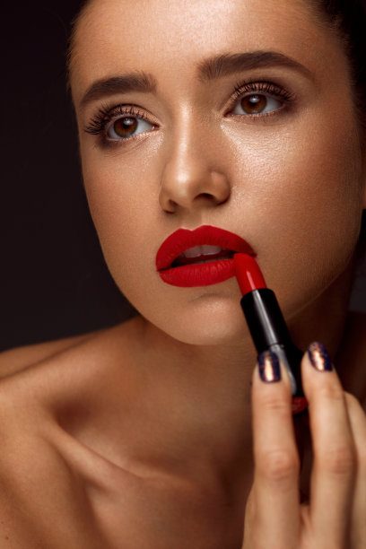 美丽的女人与明亮的红色嘴唇和口红在手图片下载