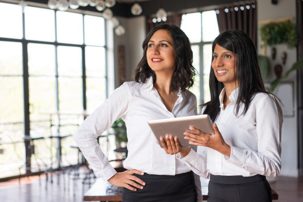 两位微笑的商务女士在咖啡馆里使用平板电脑图片下载