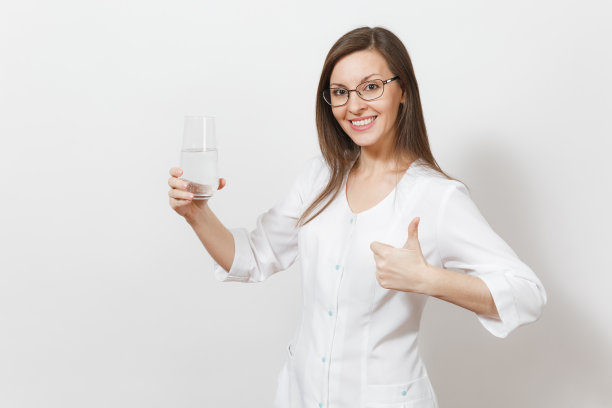 微笑美丽的医生女人孤立在白色的背景。身穿白大褂的女医生，手持水杯，翘起大拇指。医护人员、健康、医学理念。图片下载