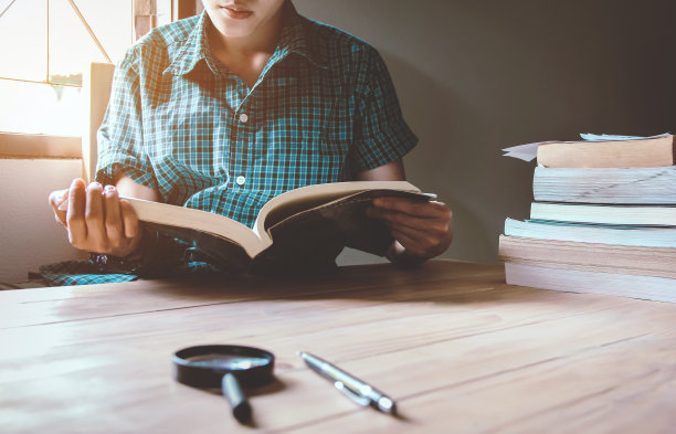 穿绿格子衬衫的男人。坐在木椅上，在桌子上看书。日落和instagram风格滤镜照片复古色调，选择性聚焦图片下载