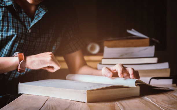 穿绿格子衬衫的男人。看着时间，坐在木椅上，在桌子上看书。日落和instagram风格滤镜照片复古色调，选择性聚焦图片下载