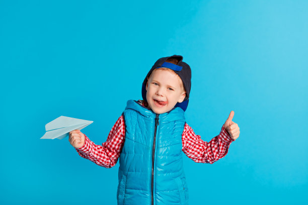 旅游概念。飞。小男孩戴着帽子玩着蓝色的纸飞机，露出舌头图片下载