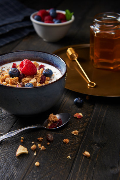 健康的早餐。新鲜格兰诺拉麦片，酸奶什锦麦片，蓝莓，覆盆子，苹果干和奇亚籽蔓越莓。深色木制背景。素材图片