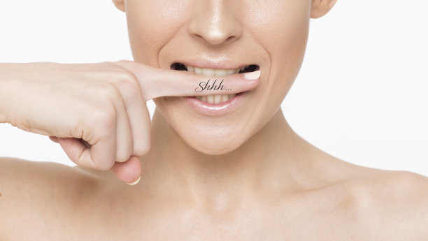 特写照片一个美丽的微笑女性的脸与干净和新鲜的皮肤，女孩把一根手指放在她的嘴唇。图片下载