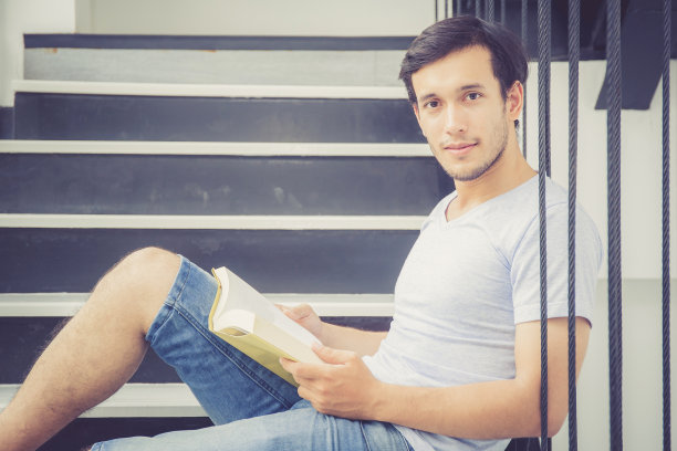 英俊年轻的商务亚洲人在休闲服装阅读书籍在客厅，教育学习知识的概念。图片下载