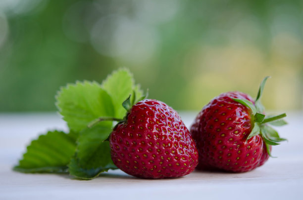 木桌上放两颗带叶子的草莓/户外照片图片下载