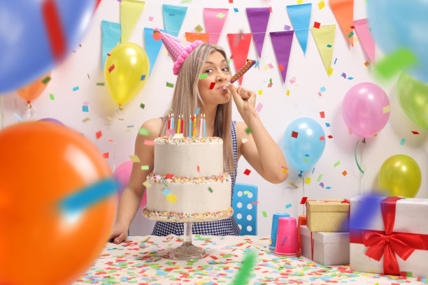 年轻女子拿着生日蛋糕吹着派对号角图片下载