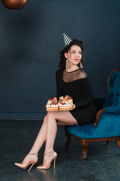 孤独的年轻女子把生日蛋糕放在膝盖上。孤立在黑色的墙壁背景图片下载