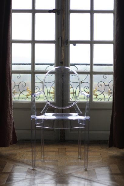 法国巴黎，一间巴黎人的房间，在法式门窗前，透过一张孤零零的玻璃/塑料幽灵椅，灯光映入眼帘。图片下载