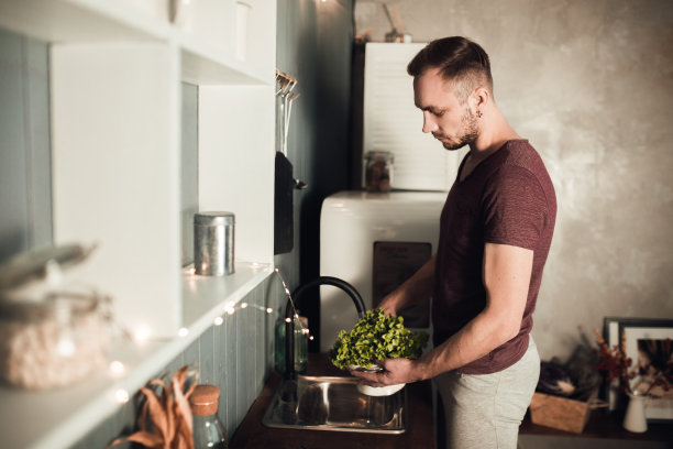 厨房里的男人。烹饪时间。乡村色彩的生活方式照片。人与健康的饮食观念。穿着运动服的家伙在厨房里洗沙拉图片下载