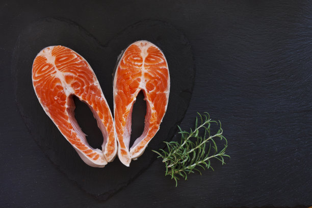 特写照片的新鲜鲑鱼与海盐和酸橙片在黑色的桌子背景。图片下载